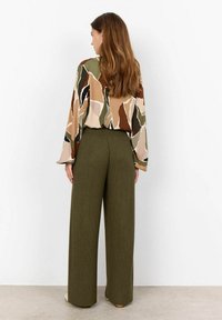 Mönstrad blus med långa ärmar i beige, grönt och brunt; tillsammans med högmidjade, olivgröna byxor med vida ben i ribbat tyg.