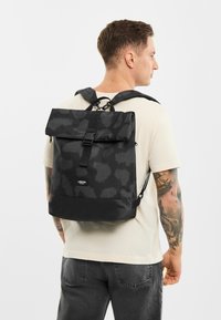 Čierny batoh s rolovacím dizajnom, jemným vzorom, nastaviteľnými popruhmi a hladkou textúrou, zabezpečený stredovým prackou.