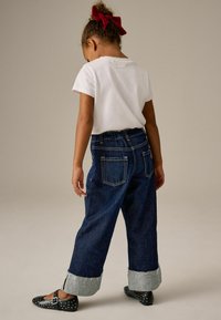 Culottes in denim con orlo sbiadito e quattro tasche, abbinati a una t-shirt bianca a maniche corte e ballerine nere con borchie argento.