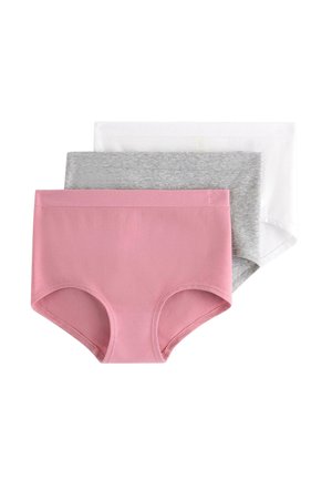 Kvinde med langt krøllet hår står barfodet iført en hvid kortærmet skjorte, der er let løftet, og grå bomuldsundertøj mod en ensfarvet hvid baggrund.