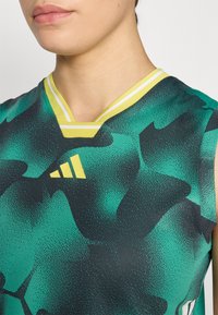 T-shirt de sport sans manches avec un motif abstrait vert et noir, des accents jaunes, et un col en V avec une double bande blanche.
