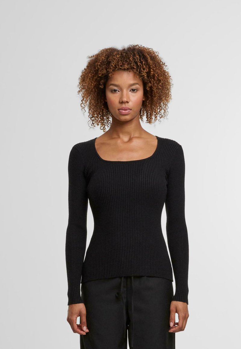 Schwarzer gerippter Langarmpullover mit quadratischem Ausschnitt, taillierter Form und strukturiertem Stoff. Kombiniert mit lockeren schwarzen Hosen.