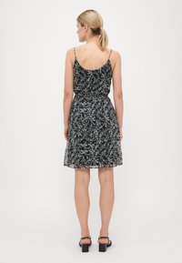 Vestido negro con flores, con tirantes ajustables, cintura fruncida y tela opaca. Presenta patrones florales blancos sobre una superficie texturizada.