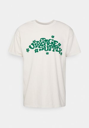 T-shirt blanc à manches courtes avec texte rétro vert « VINTAGE SUPPLY » décoré d’illustrations de fleurs vertes sur le devant.