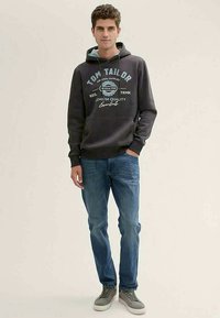 Sweat à capuche gris avec un graphique sur le devant, des accents bleus, poche kangourou, associé à un jean bleu clair et des baskets basses grises.