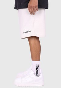 Hvide bomulds-shorts med "Dropsize" i sort tekst, parret med hvide træningssko og hvide sokker med sort branding.