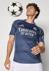 Maglietta sportiva blu navy con maniche corte, caratterizzata da dettagli verde chiaro e dal logo "Emirates Fly Better" sul davanti.