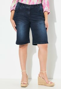 Tummansiniset farkku-bermudashortsit, joissa on viisi taskua, nappikiinnitys ja vyölenkit. Rentoa istuvuutta, hieman rispaantuneet lahkeensuut.