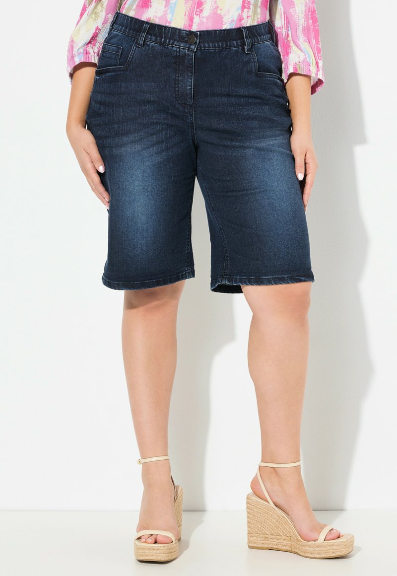 Tummansiniset farkku-bermudashortsit, joissa on viisi taskua, nappikiinnitys ja vyölenkit. Rentoa istuvuutta, hieman rispaantuneet lahkeensuut.