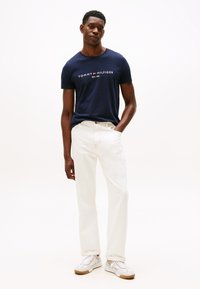 Laivastonsininen puuvillainen t-paita, jossa valkoinen "TOMMY HILFIGER EST. 1985" -logo, yhdistetty kermaan vivahtaviin farkkuihin ja valkoisiin tennareihin. Yksinkertainen, rento asu.