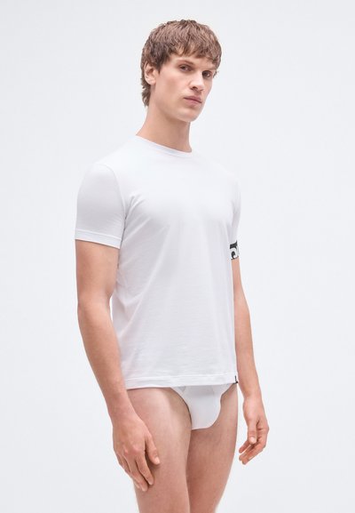 Hvid T-shirt med korte ærmer lavet af bomuldsstof, med rund halsudskæring og et sort logo på ærmet. Figurformet pasform.