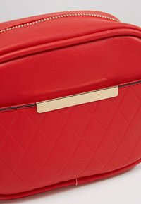 Czerwona torebka z sztucznej skóry z pikowanym wzorem, złotymi akcentami i zapięciem na zamek. Gładka faktura i zaokrąglony kształt.