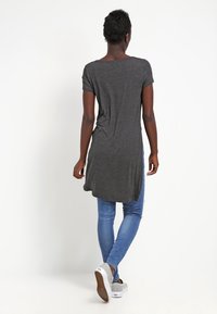 Túnica gris de manga corta con un dobladillo trasero más largo, combinada con jeans ajustados azules y zapatillas blancas, con una textura suave y ligera.