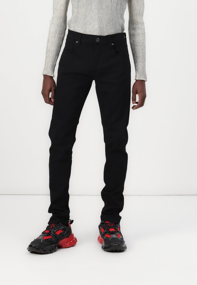 Svarta skinny jeans med femfickorsdesign, tillsammans med svarta och röda klumpiga sneakers med meshpaneler och tjocka gummisålar.