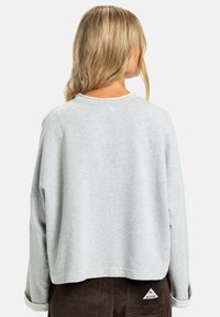 Sweatshirt court gris clair avec un col rond, des épaules tombantes et une texture douce, associé à un pantalon en velours côtelé marron foncé avec une étiquette de marque.