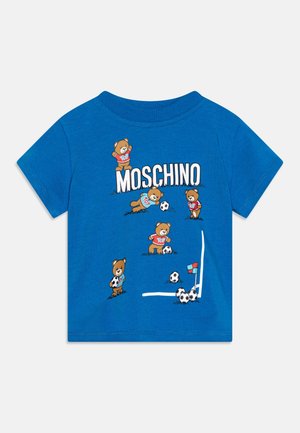 Camicia blu per bambini con logo Moschino e orsi che giocano a calcio vicino alla porta con più palloni da calcio sull'erba.