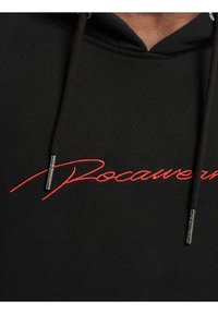 Felpa nera con cappuccio e testo ricamato rosso "Rocawear." Presenta coulisse con punte metalliche e un tessuto morbido e strutturato.