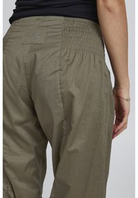 Pantaloni di colore verde oliva con vita arricciata, materiale leggero, texture liscia e etichetta del marchio ben visibile sul retro.