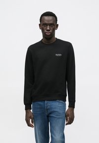 Μαύρο φούτερ από βαμβακερό μείγμα, με στρογγυλή λαιμόκοψη, ριμπ μανσέτες και τελείωμα, με μικρό λευκό λογότυπο στο αριστερό στήθος. Συνδυασμένο με μπλε τζιν.