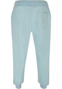 Lys blå joggebukser laget av mykt stoff, med elastisk midje, avsmalnende ben og en baklomme på høyre side.