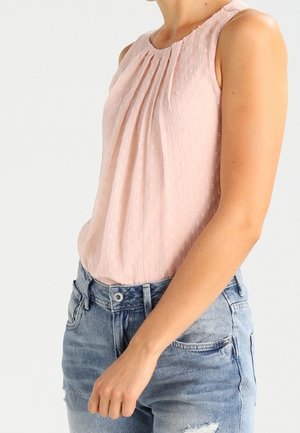 Blusa senza maniche di un delicato rosa pallido con pieghe sottili e tessuto strutturato. Abbinata a jeans in denim blu usurati.