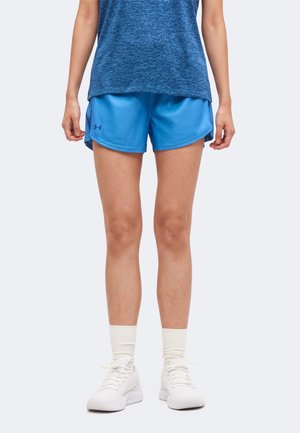 Person trägt blaue Sportshorts, blaues strukturiertes Shirt, weiße Knöchelsocken und weiße Turnschuhe, steht vor einem einfarbigen Hintergrund.