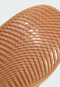 Sålen af en sko med et struktureret fiskebensmønster i blødt orange gummi, med hævede ribber for bedre greb og trækkraft.