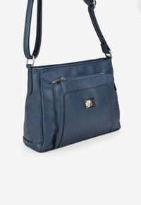 Bolso de piel azul marino tipo bandolera con correa ajustable, bolsillo con cremallera en la parte frontal y herrajes en tono plateado. Textura suave con sutiles detalles de costura.