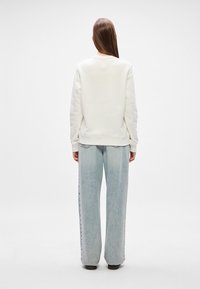 Unisex κρεμ κοντομάνικα φούτερ με στρογγυλή αξύριστη λαιμόκοψη και ριμπ μανσέτες, συνδυασμένο με ψηλόμεσες ανοιχτό μπλε φαρδιές τζιν παντελόνες με ξεθωριασμένη φινίρισμα.