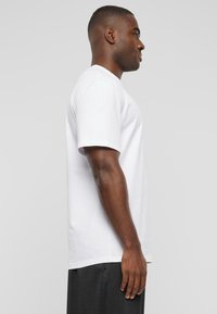 White cotton t-shirt with a crew neckline and short sleeves, shown from the side, paired with black pants, smooth texture, simple design.