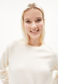 Cream-colored, lightweight sweater with a crew neckline and long sleeves, featuring a soft texture and minimal design.