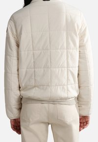 Pohodlná bombr jacket v off-white barvě, se štepovaným vzorem, žebrovaným lemem a manžetami, a minimalistickým designem bez viditelného brandingu.