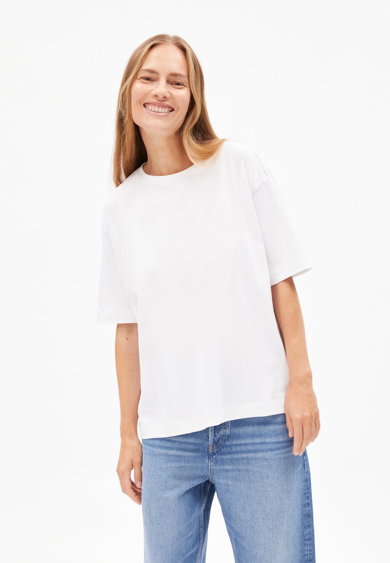 Weißes T-Shirt mit Rundhalsausschnitt und kurzen Ärmeln, aus weichem Stoff. Kombiniert mit hellblauen Jeans, die eine lockere Passform haben.
