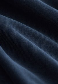 Mørkeblå tekstureret stof med fin ribstribning, der viser bløde folder og en glat overflade, velegnet til forskellige tekstilapplikationer.
