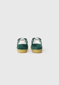 Baskets en suede vert avec des accents blancs, une texture lisse et une semelle en caoutchouc. Présentent un design basse avec des lacets et un col rembourré.