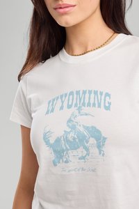 Valkoinen puuvillapaita, jossa on sininen graafinen kuva cowboysta hevosella, tekstillä "WYOMING" ja "Lännen henki."