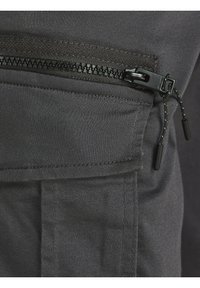 Läheltä kuvattu mustasta kangastaskusta, jossa on vaakasuora musta vetoketju ja vetoköysit tumma vaatteissa.