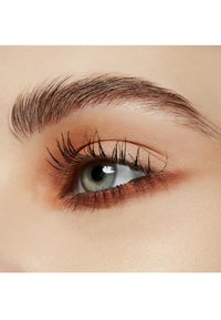 Close-up van een mensenoog toont een lichtgroene iris, lange donkere wimpers en zacht gedefinieerde bruine oogschaduw tegen een gladde huid.