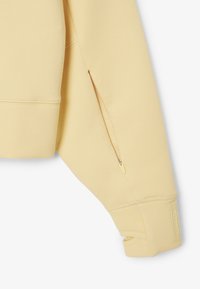 Helles gelbes Sweatshirt mit einem Reißverschlusstasche am Ärmel, geripptem Bündchen und strukturierten Details in der Nähe der Schulternaht. Glattes Material.