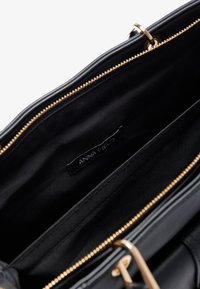 Black synthetic handbag interior with gold zipper, featuring a smooth texture. A fabric label reads "ANNA FIELD."