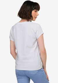 Camiseta blanca de manga corta hecha de tela suave, con un escote redondo y un corte relajado, combinada con jeans de un azul claro.