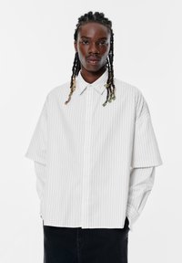 Witte gestreepte oversized blouse met knoopsluiting aan de voorkant, voorzien van brede mouwen en een klassieke kraag. Gladde stoftextuur.