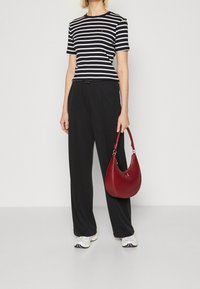 Valkoinen ja musta raidallinen puuvillapaita, löysät mustat housut ja punainen nahkainen olkalaukku. Lenkkarit, joissa on valkoinen ja musta kuvio.