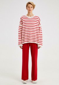 Pulover supradimensionat cu dungi roșii și albe, cu mâneci lungi, asociat cu pantaloni largi roșii. Textură netedă și design casual.