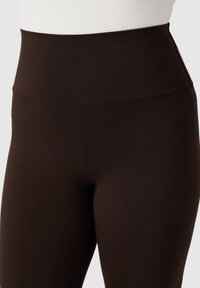 Leggings marroni a vita alta in materiale liscio ed elastico, con design senza cuciture e senza tasche visibili o decorazioni.