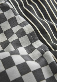 Gros plan d'un tissu à carreaux noir et blanc à côté d'un tissu noir à fines rayures blanches verticales, montrant les coutures détaillées et la texture.