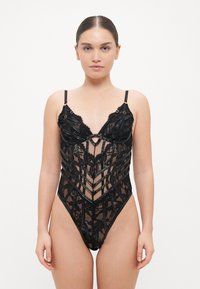 Crni čipkast bodysuit s prozirnim panelima, složenim cvjetnim uzorcima i crnim detaljima. Ima tanke podesive naramenice i duboki dekolte.