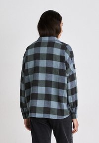 Camicia a scacchi blu e nera con colletto, maniche lunghe e polsini con bottoni. Realizzata in un morbido tessuto testurizzato. Taglio casual e orlo arrotondato.