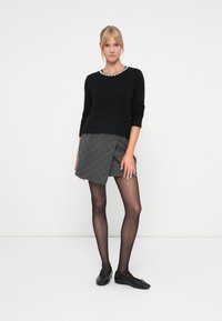 Black knitted sweater with a patterned neckline, paired with a gray checkered wrap skirt. She wears black tights and ballet flats.