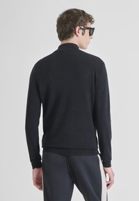 Suéter negro de punto con cuello redondo, mangas largas y puños acanalados. Textura suave con un sutil detalle de costura en los hombros.